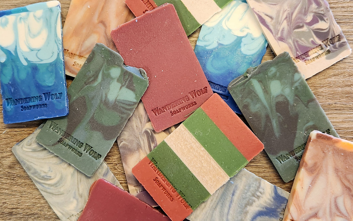 Collection of colorful soap bars with 'Wandering Wolf Soapworks' branding on a wooden surface.