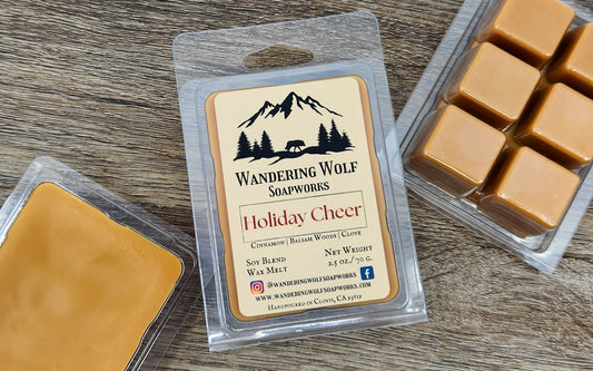 Packaging of 'Wandering Wolf Soapworks Holiday Cheer' wax melts with visible wax cubes in a clear plastic clamshell. The label on the package has a Christmas-themed design.