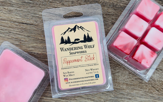 Packaging of peppermint stick wax melts with visible wax cubes outside the package, with a label that reads 'Wandering Wolf Soapworks - Peppermint Stick'. The background is a wooden surface.