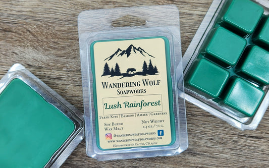 Wax melts in a packaging labeled "Lush Rainforest" with the logo of 'Wandering Wolf Soapworks' on a wooden surface.