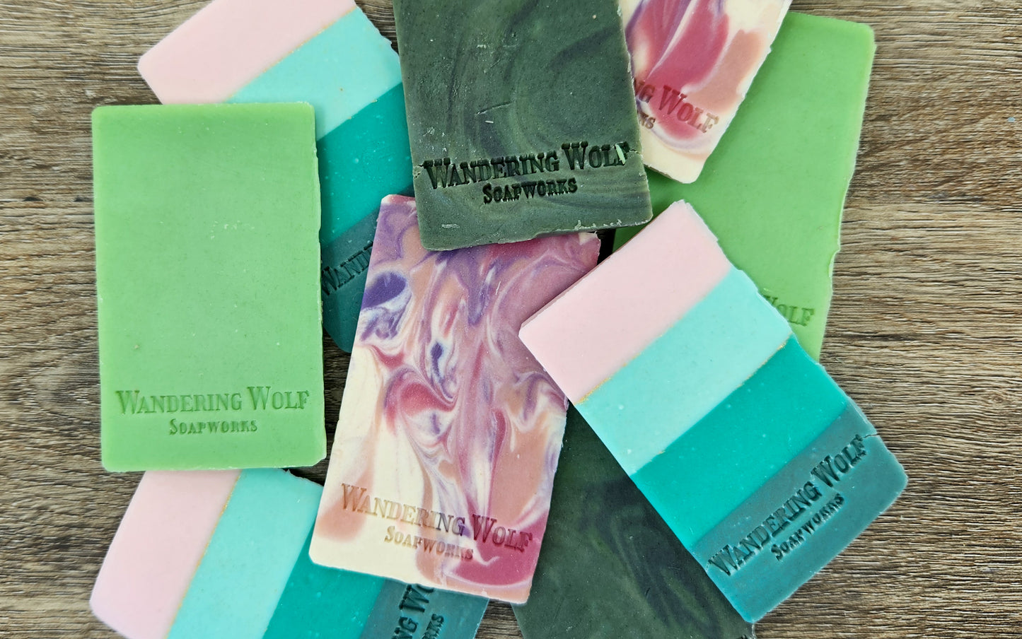 Collection of colorful soap bars with 'Wandering Wolf Soapworks' branding on a wooden surface.