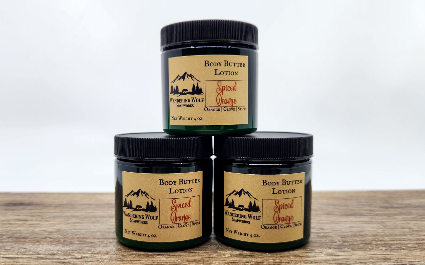 Three jars of 'Spiced Orange' body butter lotion on a wooden surface with a white background