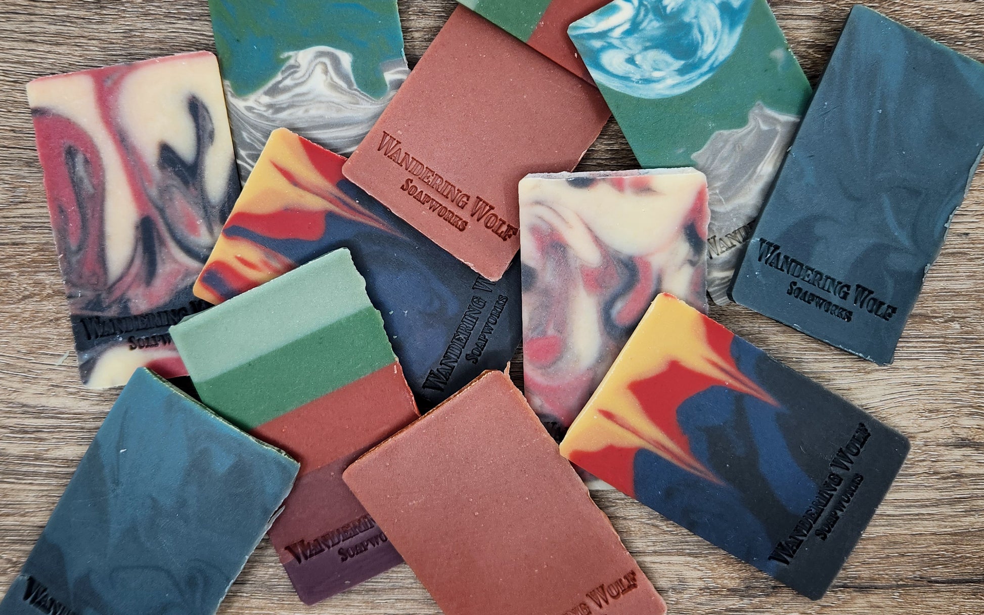 Collection of colorful soap bars with 'Wandering Wolf Soapworks' branding on a wooden surface.