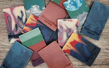Collection of colorful soap bars with 'Wandering Wolf Soapworks' branding on a wooden surface.